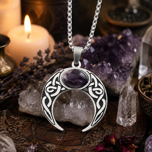 Silver Celtic knot crescent moon necklace with amethyst gemstone pendant resting on a raw quartz crystal cluster, surrounded by amethyst points and a lit candle