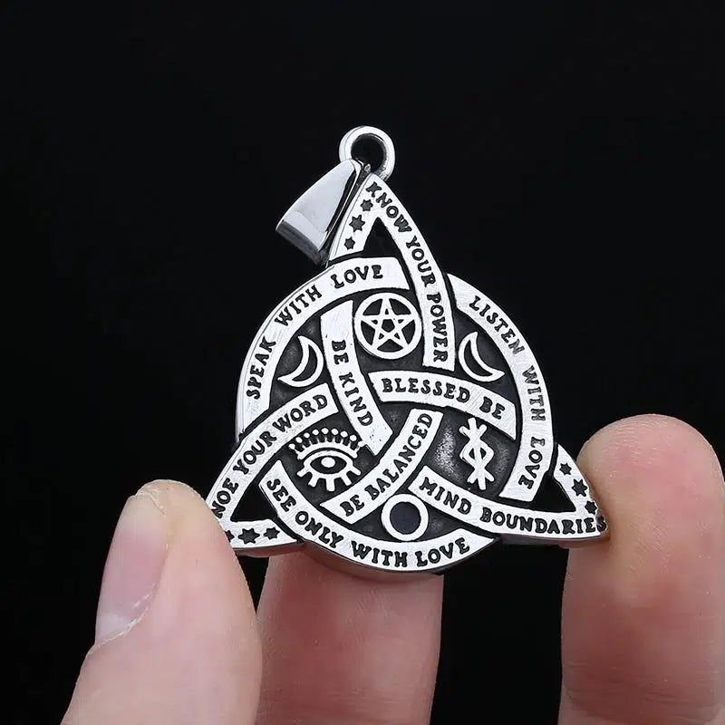 Silver Triquetra Celtic Knot Necklace with Wiccan symbols and empowering words, held by fingers.