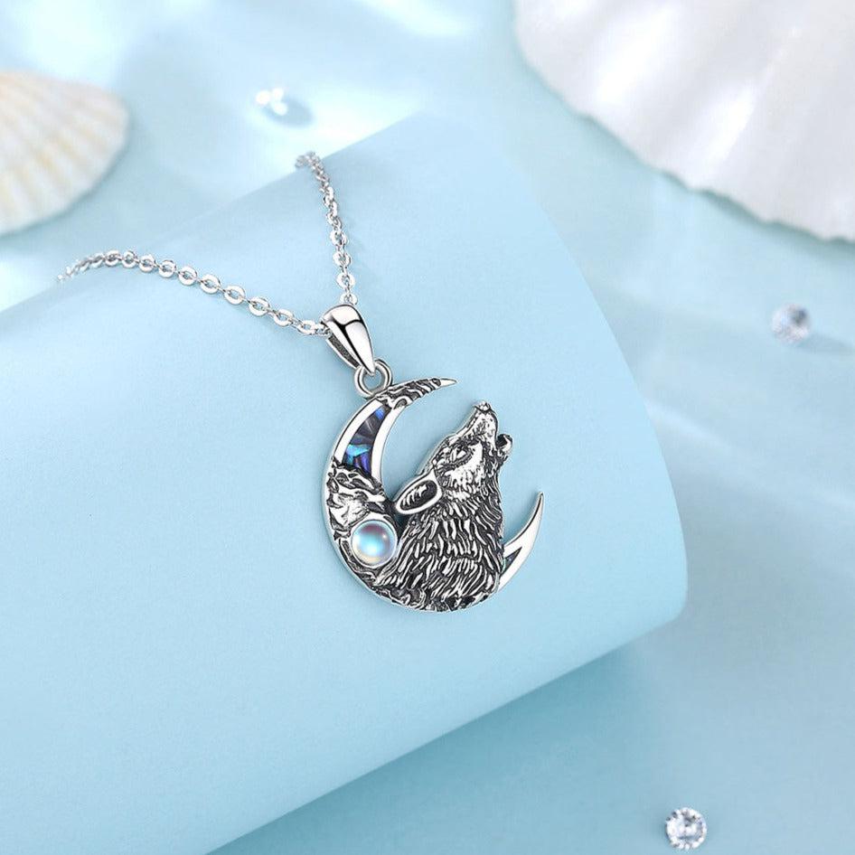 Sterling silver wolf howling at a crescent moon pendant with iridescent moonstone and abalone shell accents.