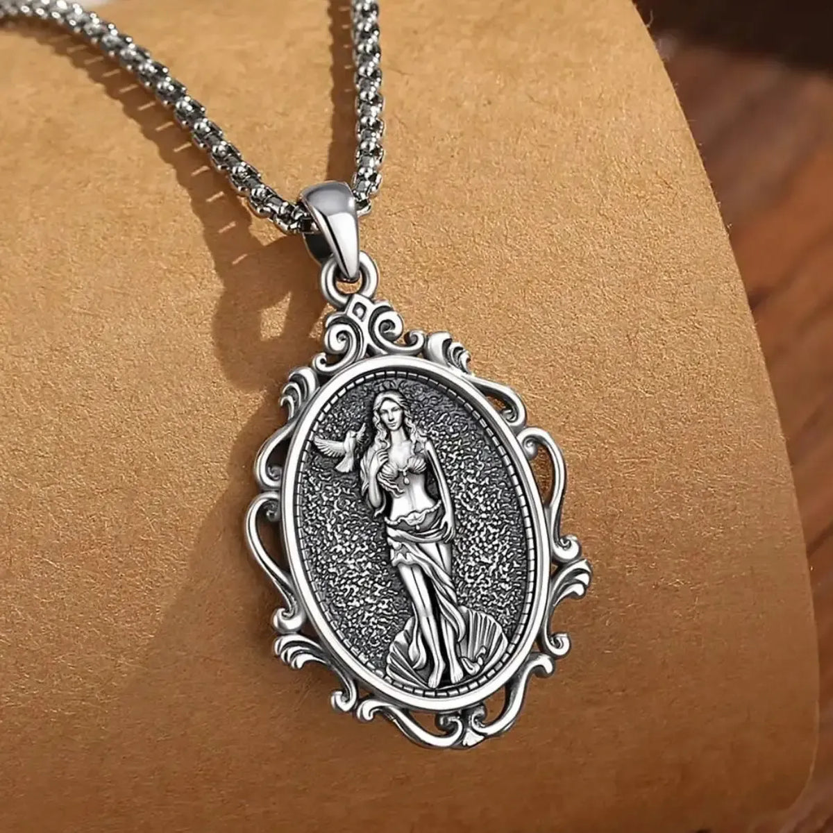 Aphrodite goddess necklace with ornate oval frame displayed on a brown box