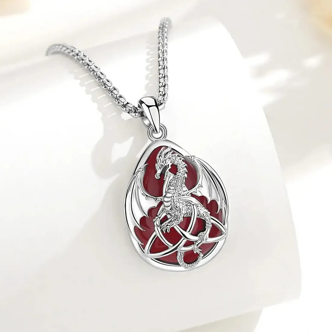 Carnelian dragon pendant with Celtic knotwork hanging from a chain over a white block