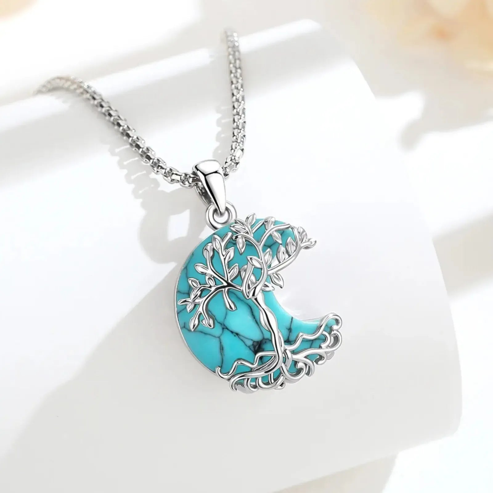 Turquoise Tree of Life crescent moon necklace displayed on white surface with soft floral background