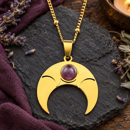 Gold-tone amethyst crescent moon pendant necklace on a witchy altar