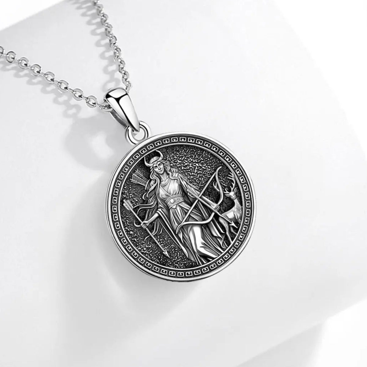Front pendant on pale fabric: Artemis Goddess Necklace in 925 Sterling Silver, featuring Artemis with a bow and deer, framed in an antique-style round pendant.