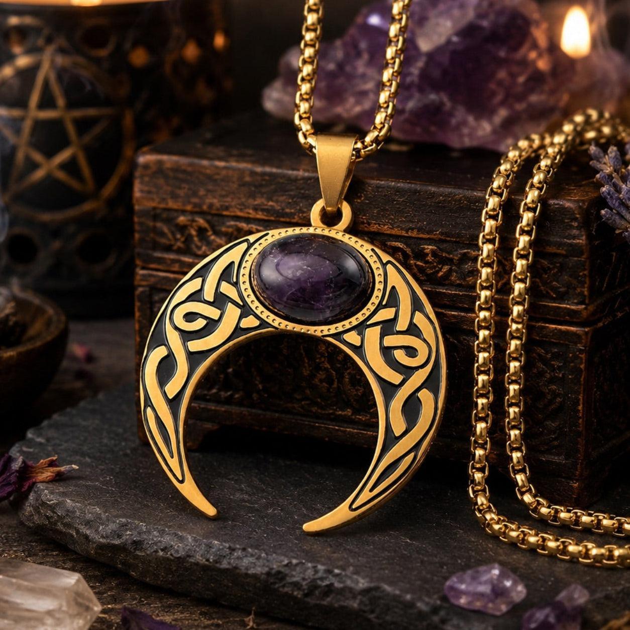 Gold Celtic knot crescent moon necklace with amethyst gemstone pendant and coiled box chain, displayed on a carved wooden box with amethyst crystals and a pentagram candle holder