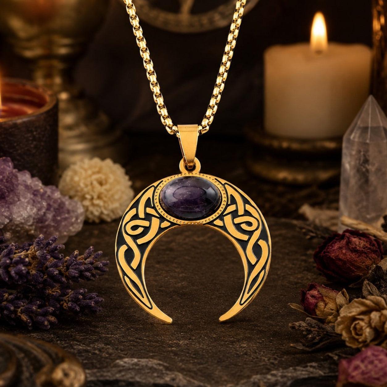 Close-up of gold Celtic knot crescent moon necklace with oval amethyst cabochon pendant, styled with amethyst clusters, a clear quartz point, dried flowers, and a lit candle