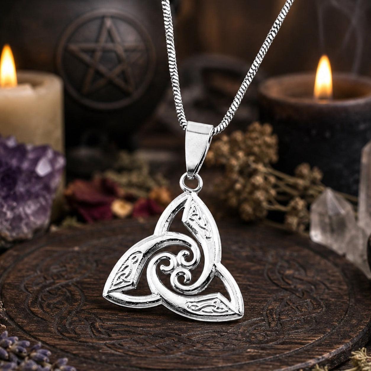 Silver Celtic triquetra trinity knot pendant necklace on curb chain, styled on dark carved wooden altar with pentagram, lit candles, amethyst crystal, and dried flowers