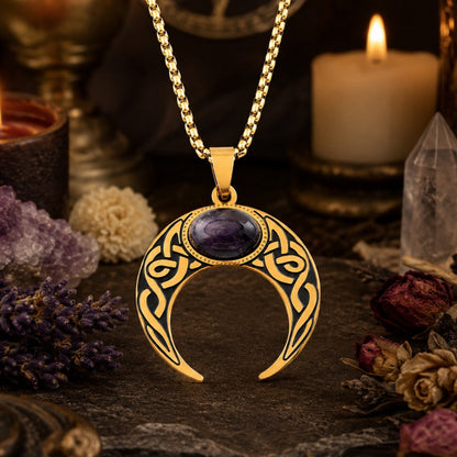 Close-up of gold Celtic knot crescent moon necklace with oval amethyst cabochon pendant, styled with amethyst clusters, a clear quartz point, dried flowers, and a lit candle