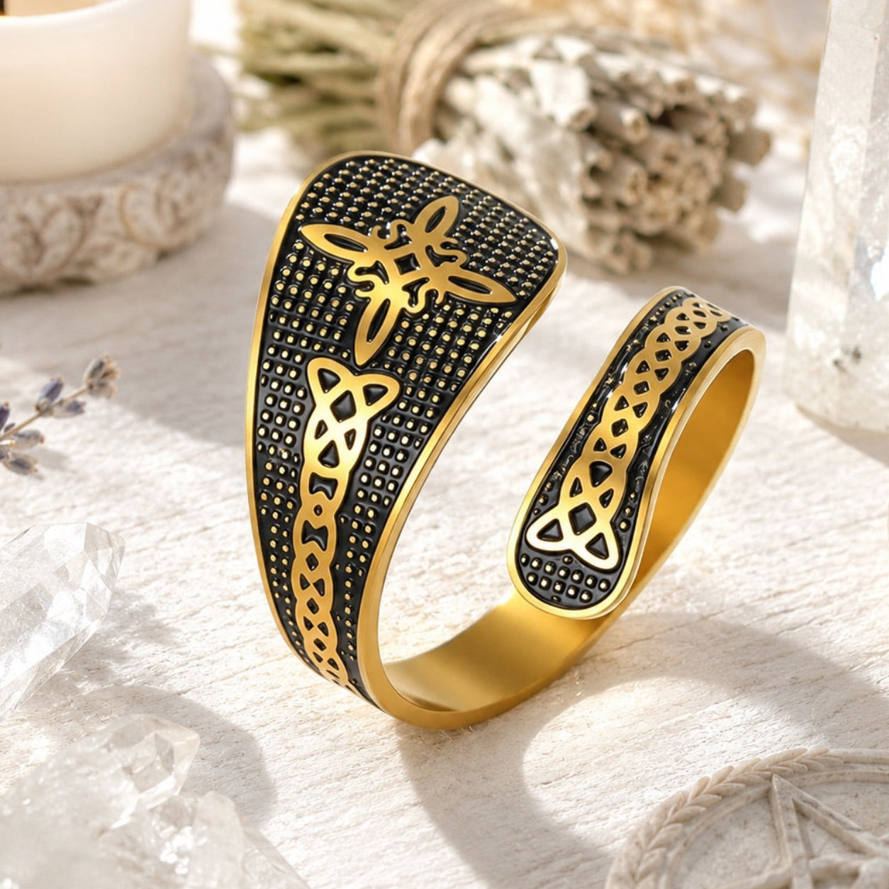 Gold Witch Knot open ring featuring Celtic trinity and endless knot engravings on a textured black band, styled with candles and dried lavender