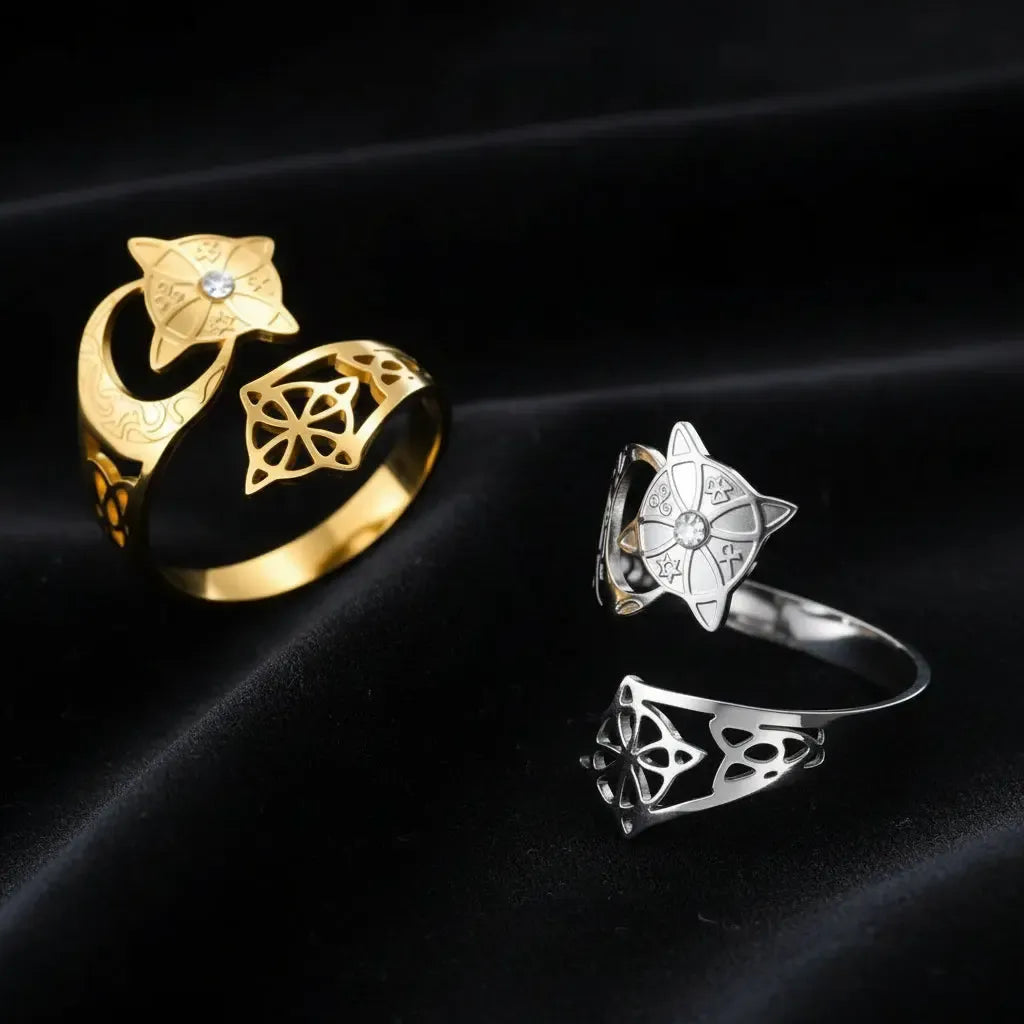 Crescent Moon Celtic Knot Ring in gold and silver on dark textured fabric, the gold ring lying flat and the silver ring standing upright, each with a star medallion, clear stone, and open celtic knot cutout design.