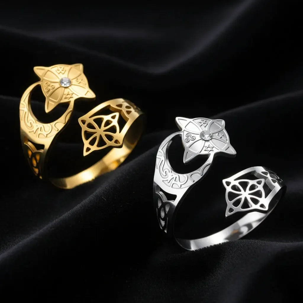 Crescent Moon Celtic Knot Ring shown in gold and silver, each featuring a star medallion set with a clear stone, an engraved crescent moon band, and an open celtic knot cutout, displayed together on black satin fabric.
