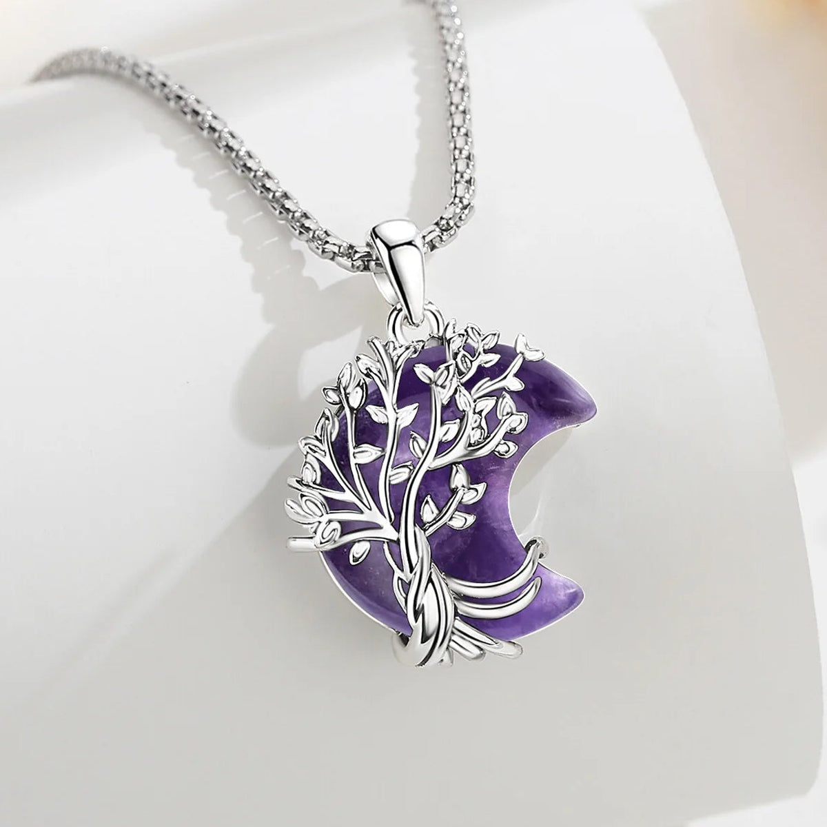 Crescent necklace styled on pale fabric: Crescent Moon Tree of Life Necklace, featuring a branching tree of life over a crescent-shaped stone.