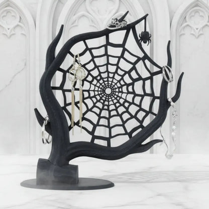 Black spider web jewelry stand with earrings on a white background