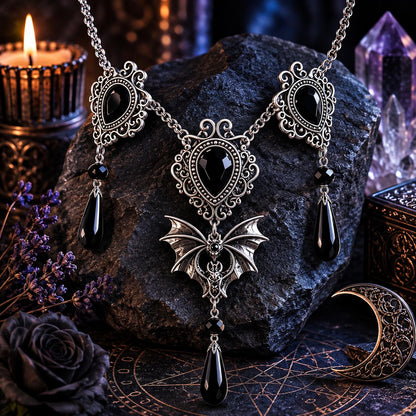 Gothic-style necklace with bat pendant on a dark stone surface with candles and crystals.