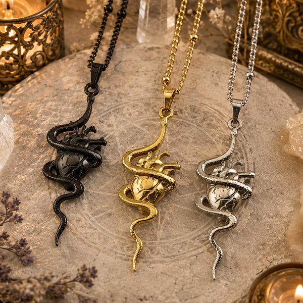 Three snake-shaped necklaces in black, gold, and silver on a textured surface with candles and crystals.
