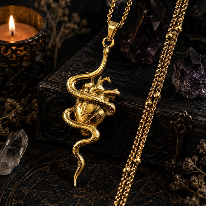 Gold snake pendant necklace on a dark background with candles and crystals.