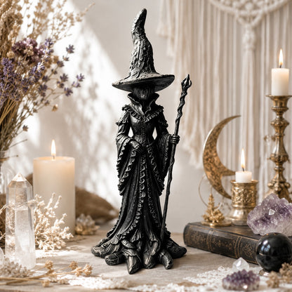 Gothic witch statue in flowing robe near golden candlesticks and crescent moon decor