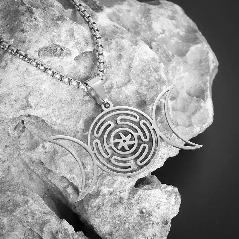 Striking stainless steel Hecate Wheel Triple Moon necklace, a powerful Wicca symbol on a textured rock.