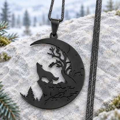 Black stainless steel Howling Wolf Crescent Moon Necklace with tree cutouts and black chain on pale stone with a soft woodland background.