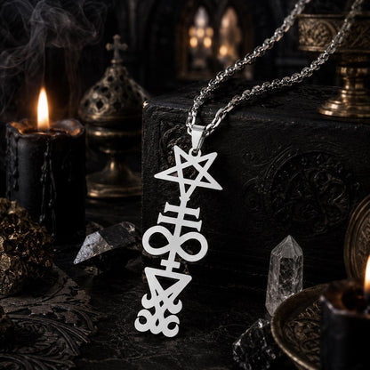 Silver Inverted Pentagram Cross sigil pendant necklace on rope chain, resting on a dark textured box with a lit candle, quartz crystal points, and ornate gothic urns