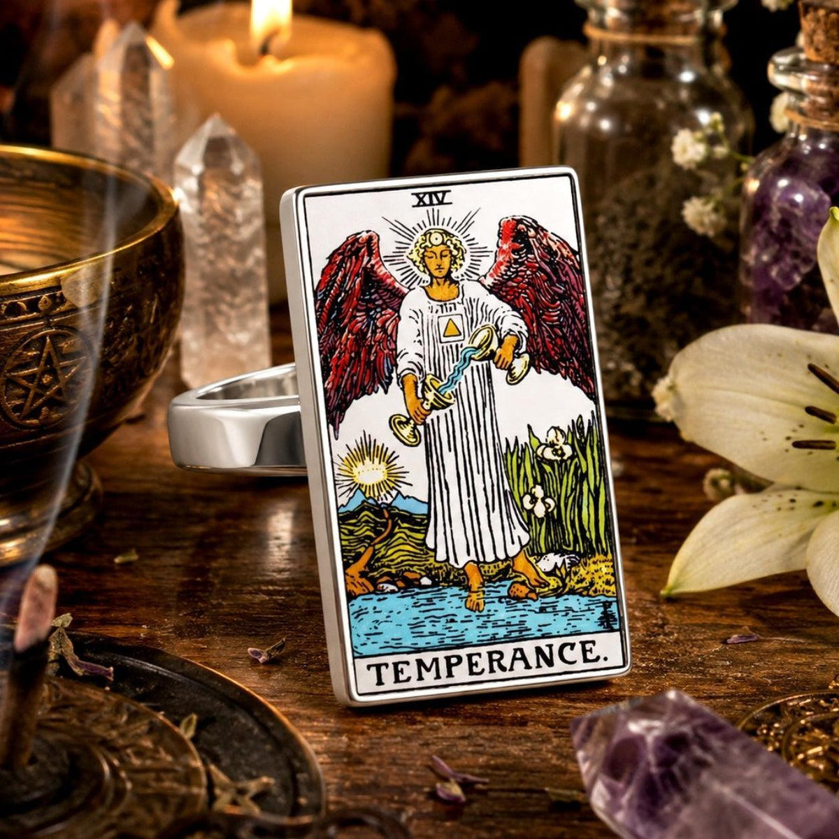 Temperance tarot card ring in stainless steel beside a goblet, candle and white lily on dark wood