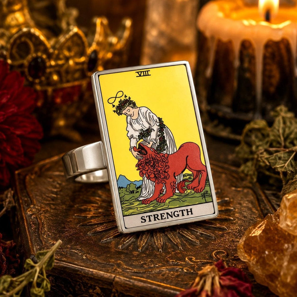 Strength tarot card ring in stainless steel beside dark red flowers, candles and antique books