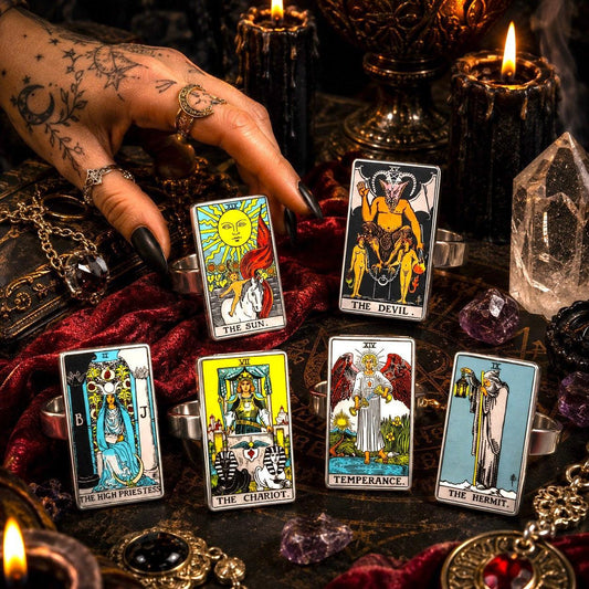 Hand wearing stainless steel tarot rings above The Sun, The Devil and High Priestess ring cards by candlelight