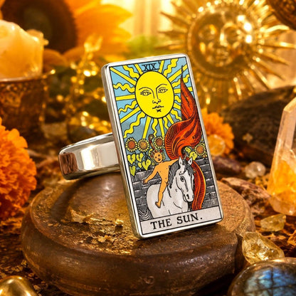 The Sun tarot card ring in stainless steel on a wooden pedestal with marigolds and warm candlelight