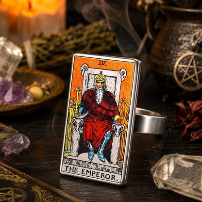 The Emperor tarot card ring in stainless steel on a dark altar with a pentacle bowl and dried roses