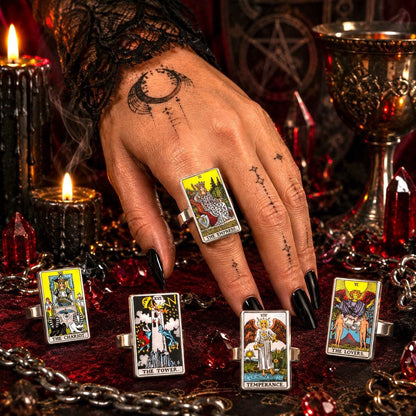 Tattooed hand wearing a Major Arcana tarot ring surrounded by tarot card rings, candles and dark crystals
