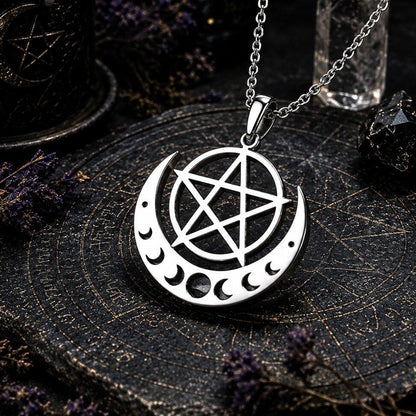 A silver-toned metal pendant necklace featuring a crescent moon with inner moon cutouts and a pentagram in the center, hanging from a chain on a dark mystical surface with occult-themed props.