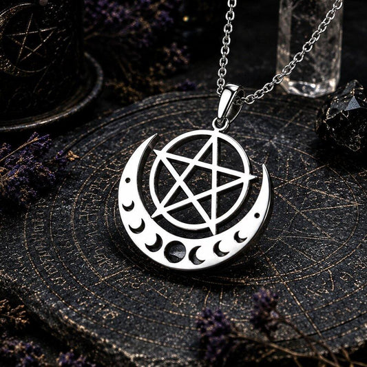 A silver-toned metal pendant necklace featuring a crescent moon with inner moon cutouts and a pentagram in the center, hanging from a chain on a dark mystical surface with occult-themed props.
