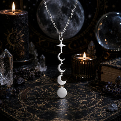 A silver-toned necklace with a vertical triple-moon-and-circle pendant hangs on a dark occult-themed surface surrounded by candles, crystals, and moon-gazing props.