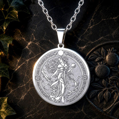 A silver pendant necklace featuring an intricately engraved circular design of a classical female figure, displayed on a dark textured surface with decorative ivy leaves.