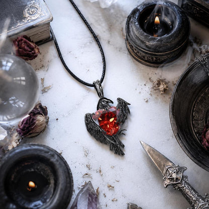 Necklace with a red gemstone pendant on a mystical table with candles, crystals, and books.