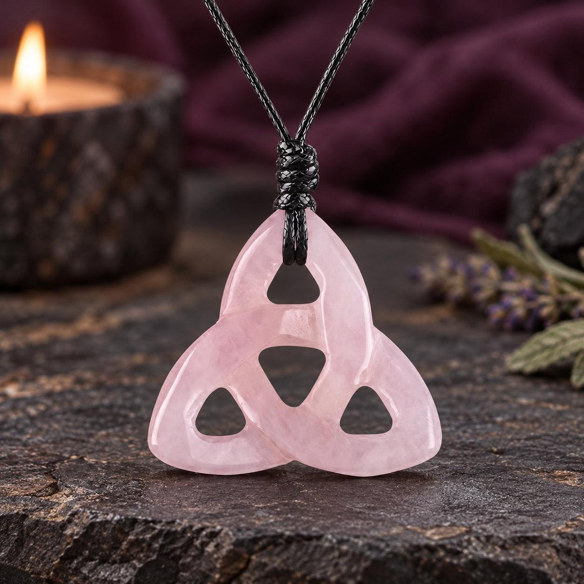 Pale pink triquetra stone pendant on a knotted cord in a witchy altar setting