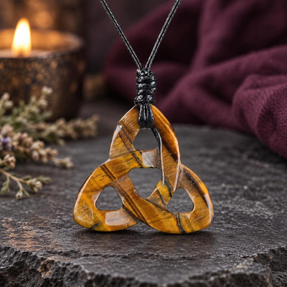 Pale pink triquetra stone pendant on a knotted cord in a witchy altar setting