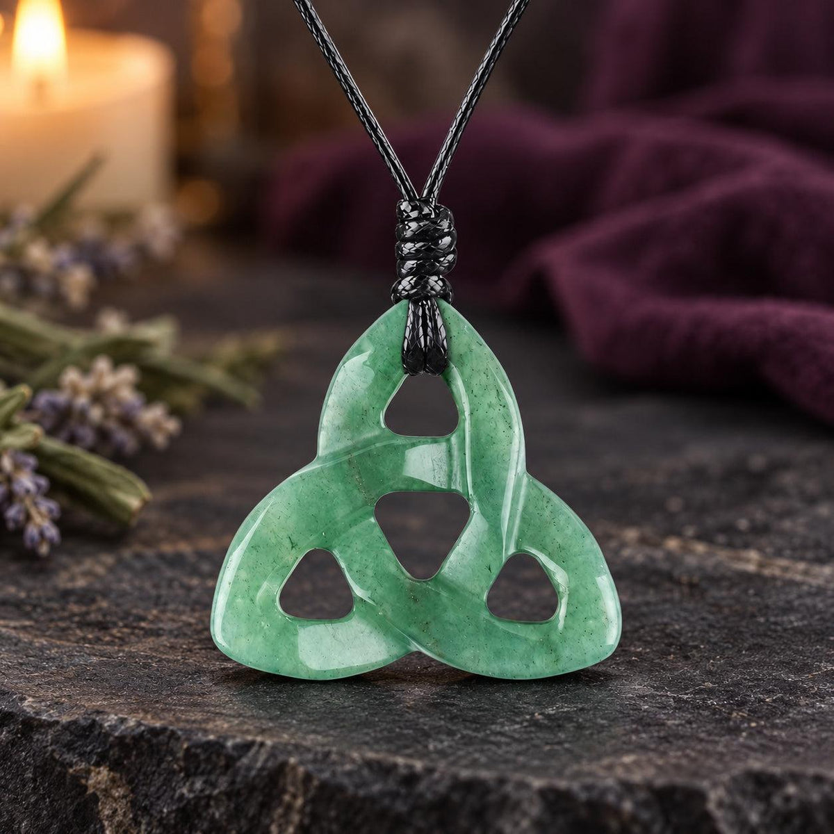 Purple and pale marbled triquetra stone pendant on a knotted cord in a witchy altar setting