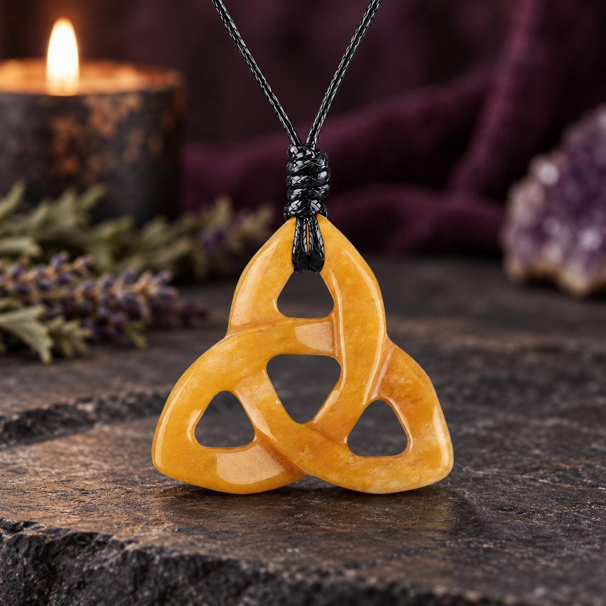 Deep reddish brown triquetra stone pendant on a knotted cord in a witchy altar setting