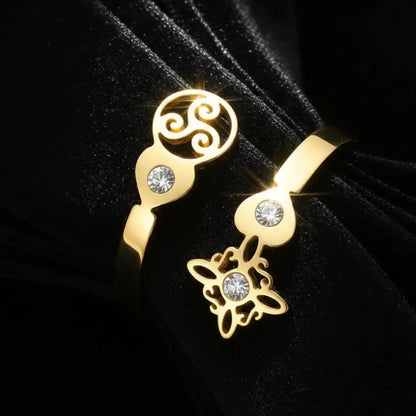 Angled close-up of gold Triskele Triple Spiral open band ring with Celtic witch knot charm and zircon stones