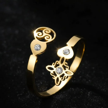Gold Triskele Triple Spiral open ring close-up on sparkling black fabric with Celtic witch knot charm and zircon accents