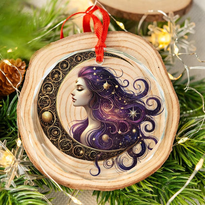 Clear glass ornament with a celestial goddess, purple hair, golden moon, and stars, hanging on a pine branch.