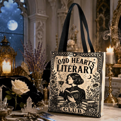 Gothic witchy tote bag printed with "Odd Hearts Literary Club" text and an art nouveau illustration of a woman holding a heart-shaped book and teacup, beside stacked books and flowers.