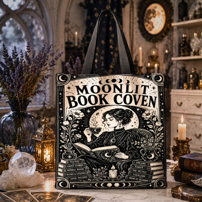 Gothic witchy tote bag printed with "Moonlit Book Coven" text and an art nouveau illustration of a woman reading by candlelight with stacked books and moon phases.
