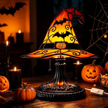 Witch hat table lamp glowing orange with bat cutouts near pumpkins and candles