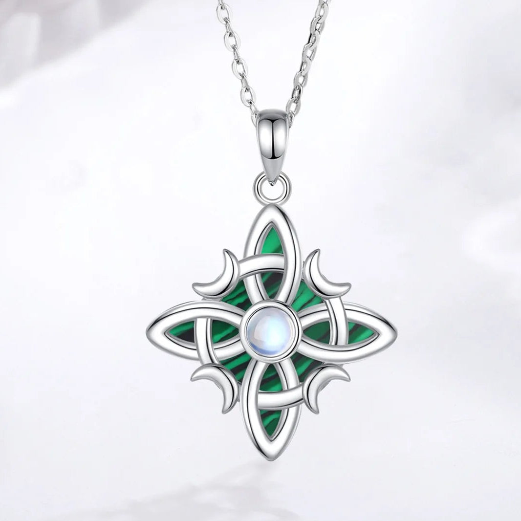 Pendant and chain on pale fabric: Witch Knot Necklace in 925 Sterling Silver, featuring an interwoven witch knot, malachite detail and an artificial moonstone center.