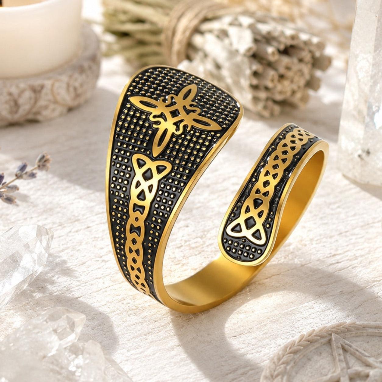Gold Witch Knot open ring featuring Celtic trinity and endless knot engravings on a textured black band, styled with candles and dried lavender