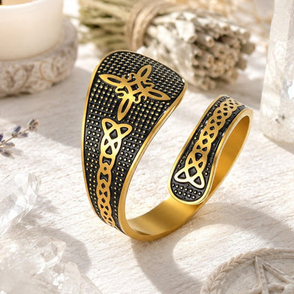 Gold Witch Knot open ring featuring Celtic trinity and endless knot engravings on a textured black band, styled with candles and dried lavender