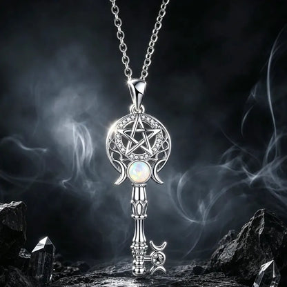A silver key-shaped pendant necklace with a pentagram design, moon crescents, and an iridescent opal-like center stone, hanging against a dark smoky background with rocks at the bottom.