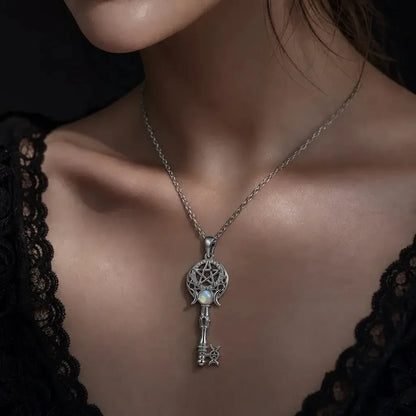 A close-up of a model wearing a silver key pendant necklace with a small white pearl accent, styled with a black lace top.